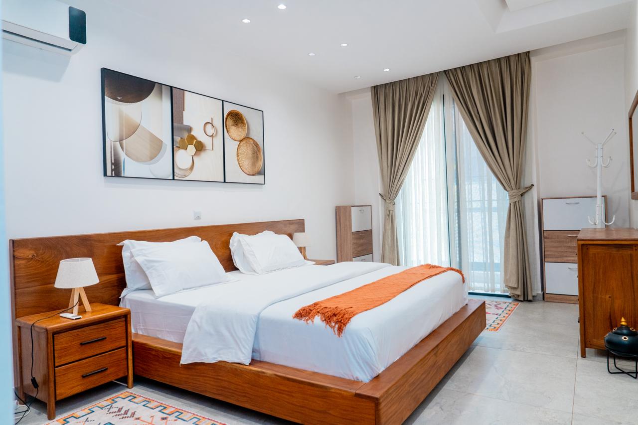 Chambre principale de l'appartement, lit en bois et rideaux beiges